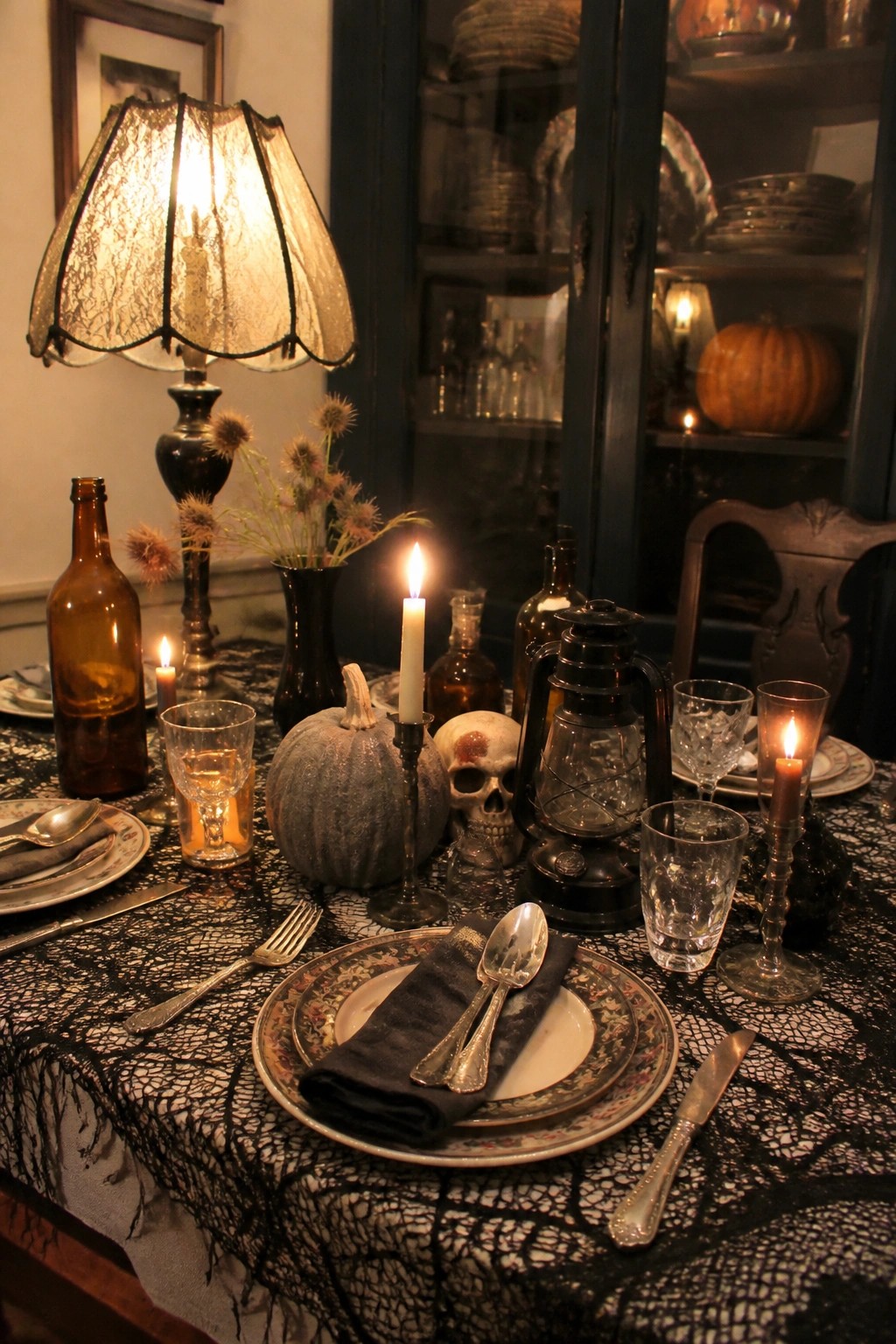 Dining table with black lace cloth, skeleton and skull centerpiece, lit candles, and dark glassware.