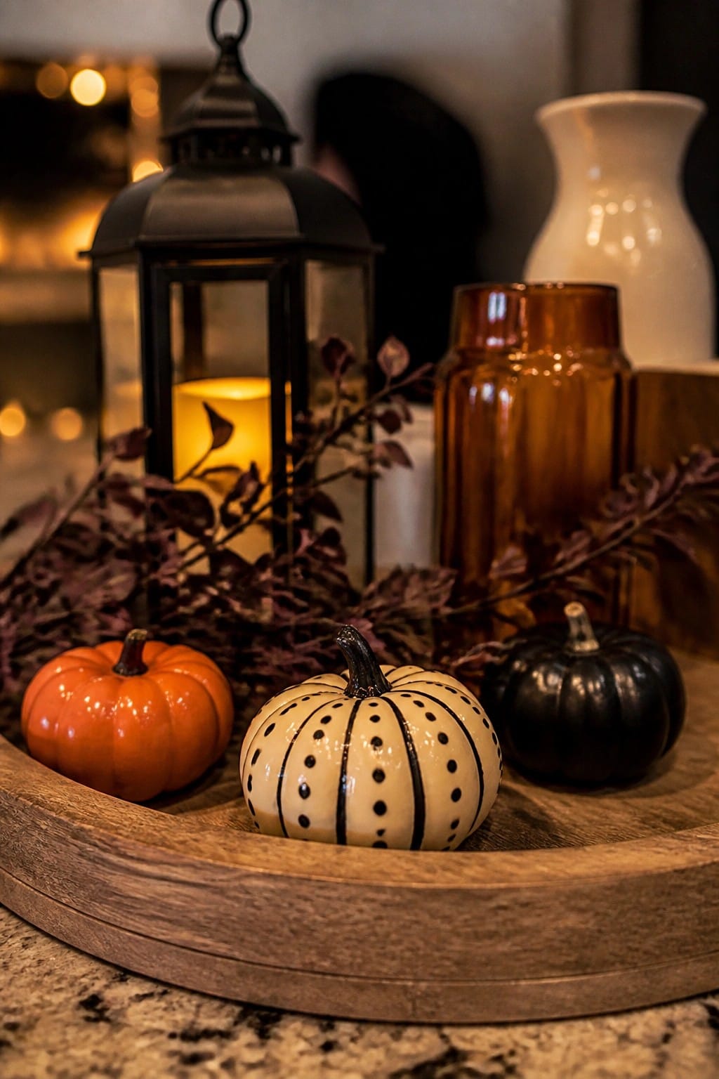 Orange, black, and polka-dotted pumpkins with lit lantern and vases on wooden tray.