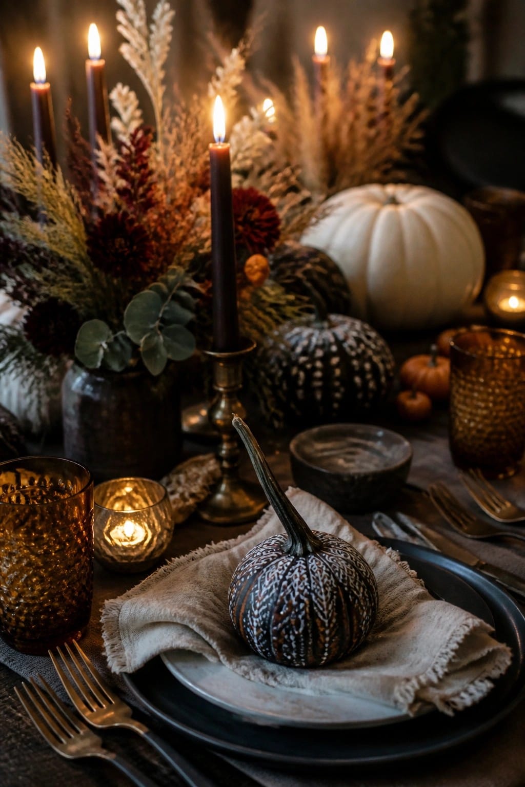 Dining table with a painted mini pumpkin placed on a plate as the main focal point, surrounded by candles, dark plates, and neutral linens.