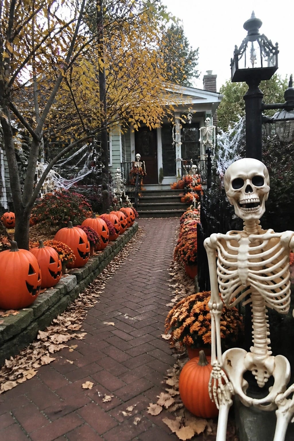 A brick walkway lined with carved jack o lanterns and plastic skeletons leading toward a house porch decorated for Halloween.