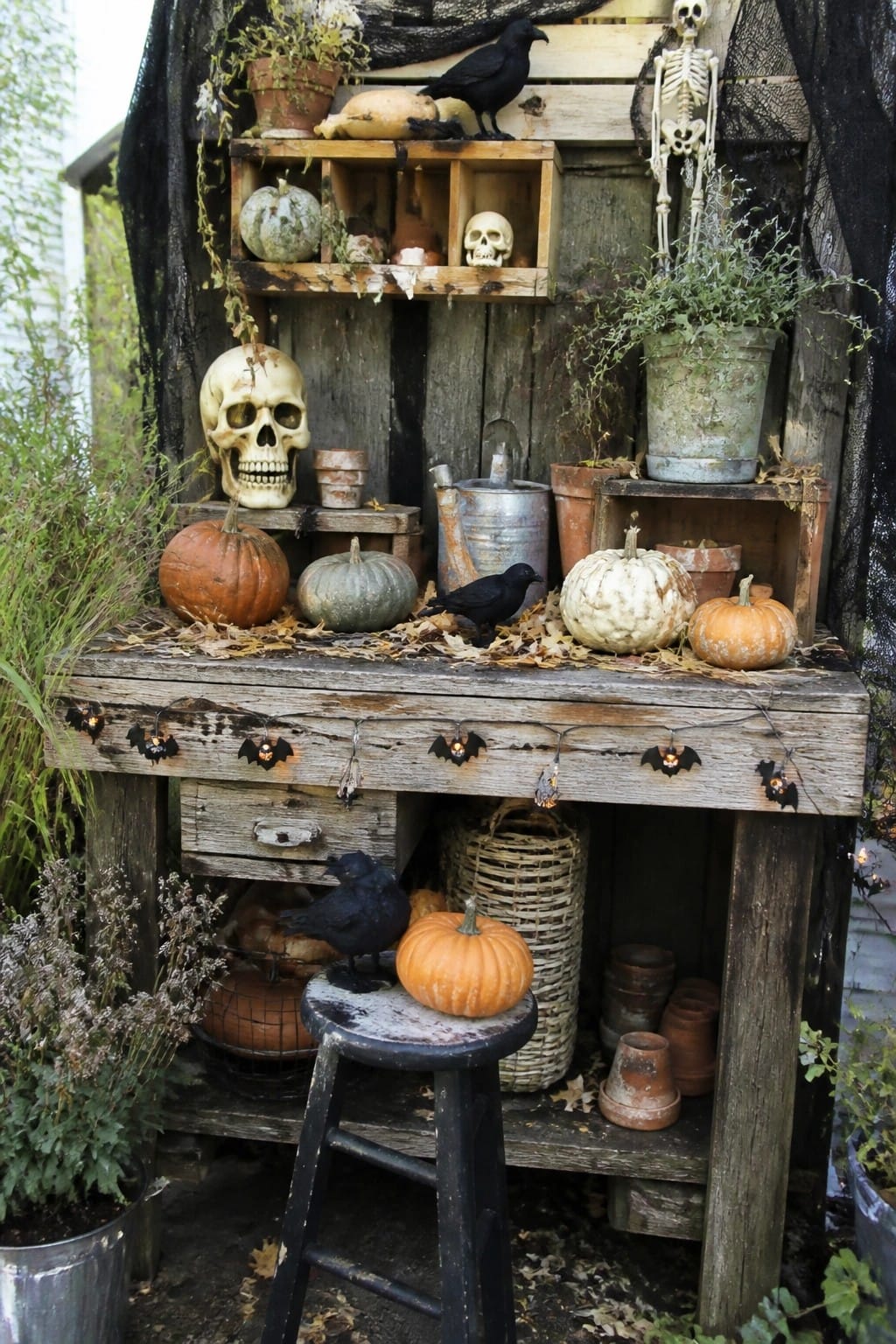 Outdoor wooden table styled with skulls, black crows, pumpkins, and bat string lights for Halloween.