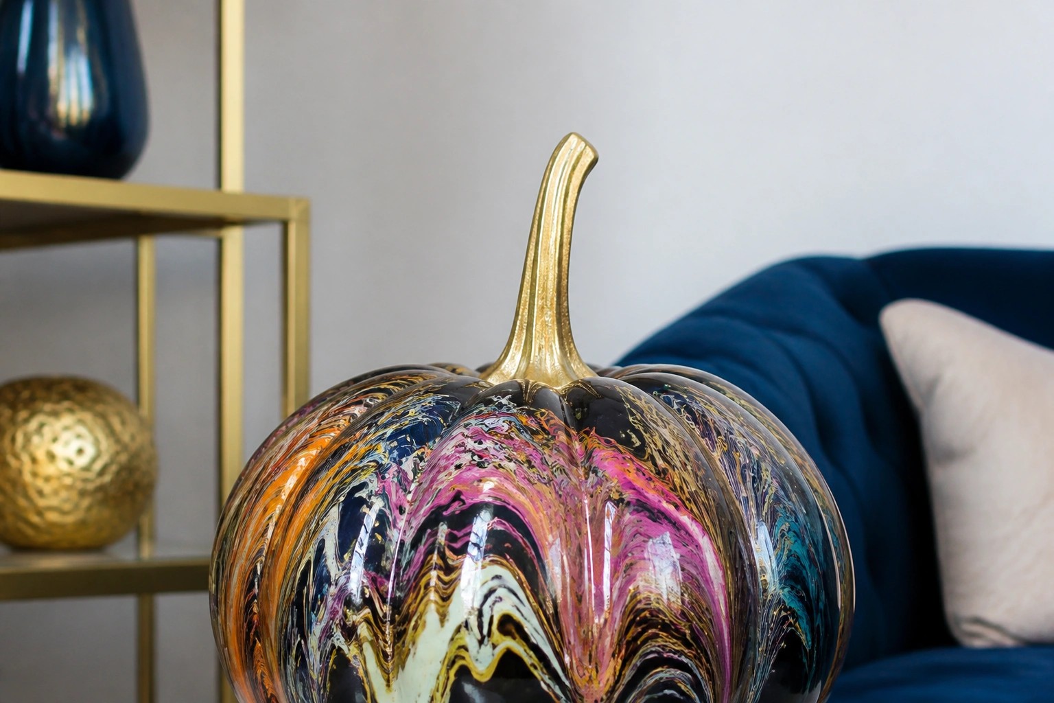 Colorful abstract-painted pumpkin with gold stem on stacked books beside black vases.