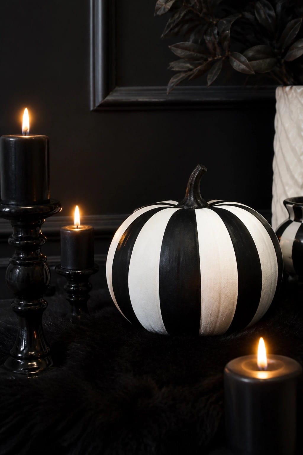 A large pumpkin painted with bold black and white vertical stripes sits among several lit black candles on a dark surface.