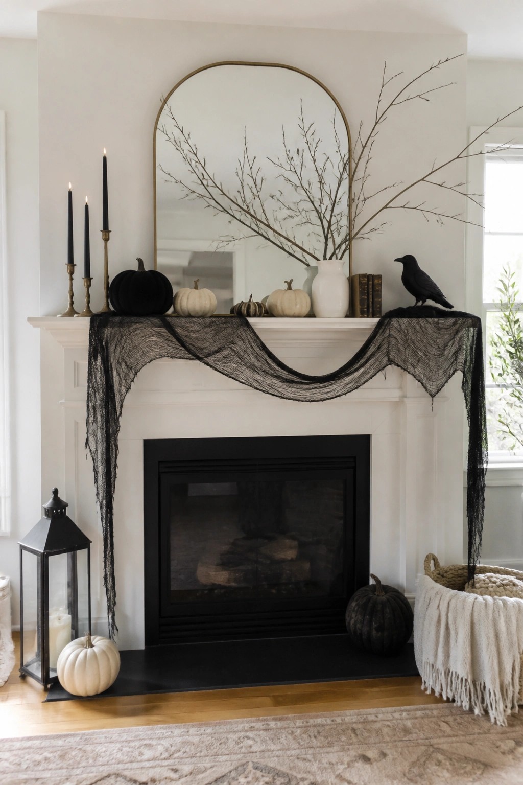 White fireplace mantel with black lace fabric draped across the front, a black crow on the right side, bare branches, and assorted white and black pumpkins.