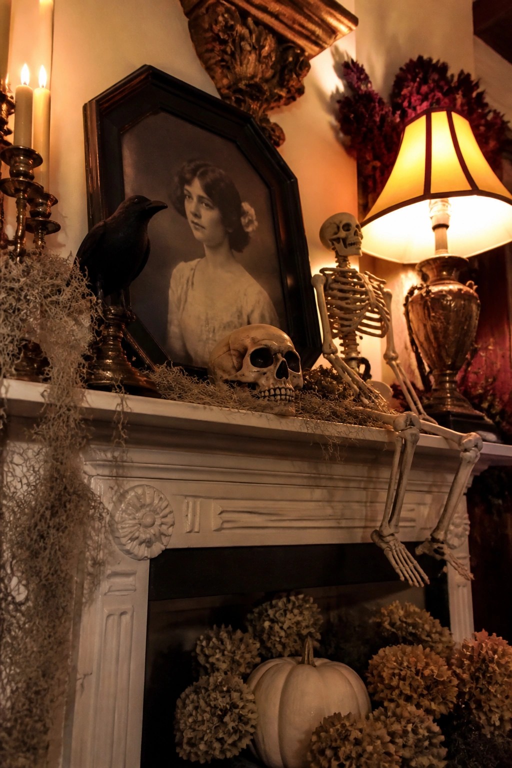 White fireplace mantel styled for Halloween with a posed skeleton, skulls, a black crow, and a vintage portrait.