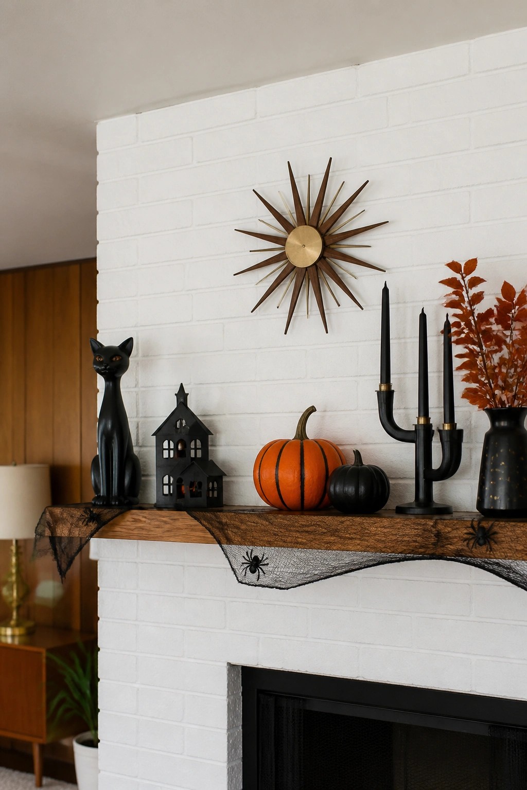 White brick fireplace mantel styled with a black cat, haunted house, orange and black pumpkins, black candelabra, and spiderweb runner.