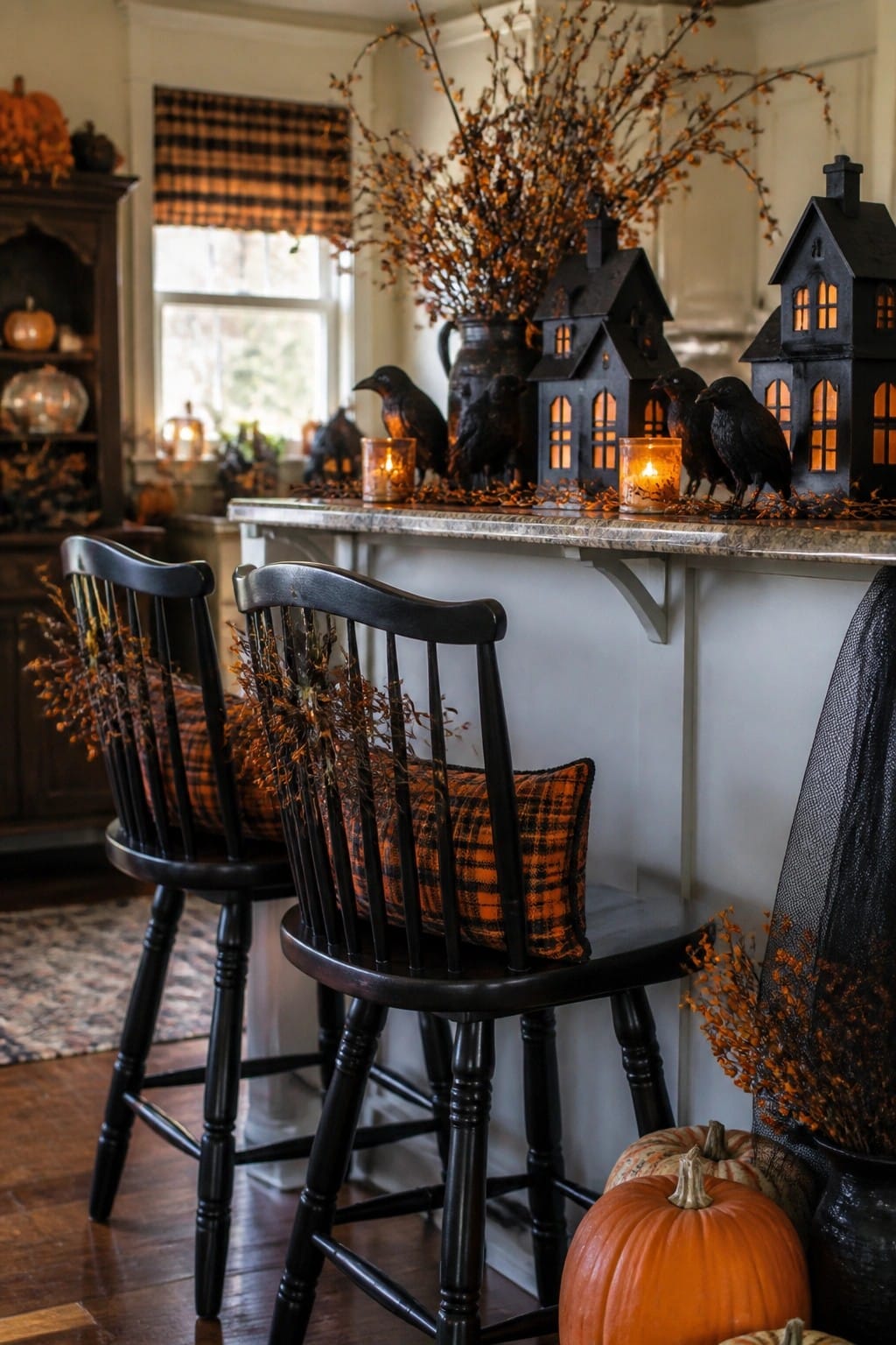 Kitchen counter with black crows and glowing black house lanterns arranged between two black stools with orange plaid pillows.