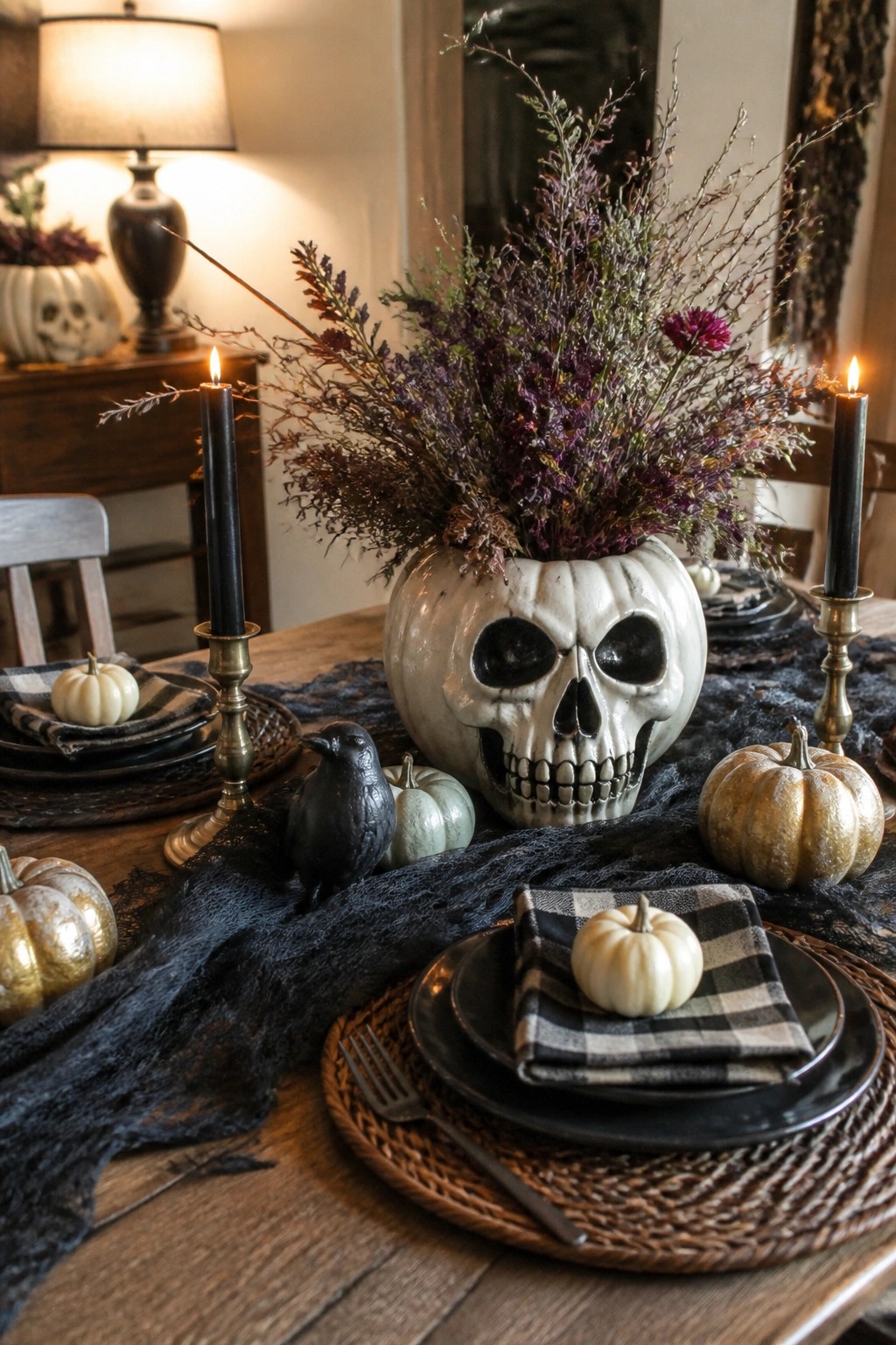 Halloween table with skull vase centerpiece, lit black candles, gold pumpkins, and crow figurine.