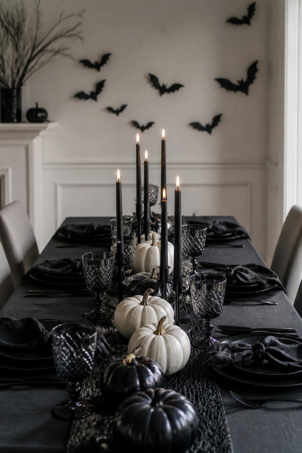 Elegant black Halloween table with lit candles, pumpkins, and bat wall decor