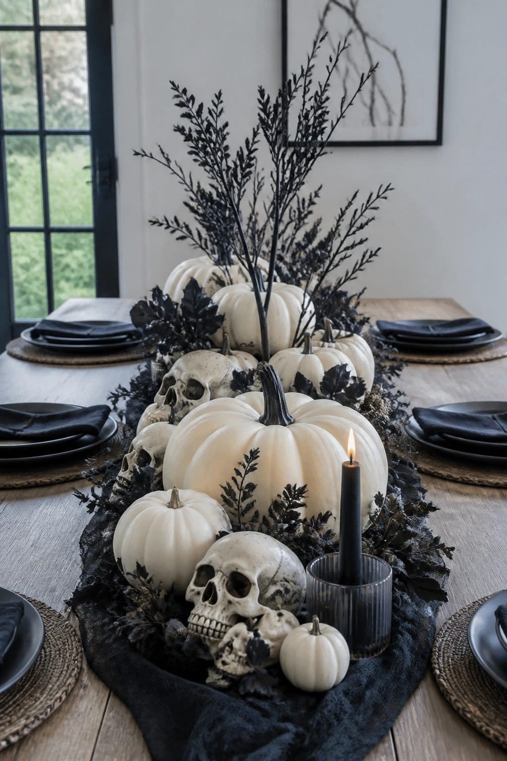 White pumpkins, skulls, black foliage and lit candle on wooden dining table
