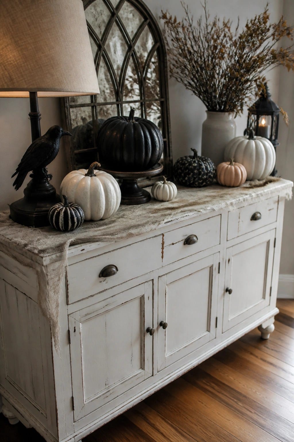 White console table styled with black, white, and striped pumpkins, a black crow figurine, and gauze fabric for Halloween.